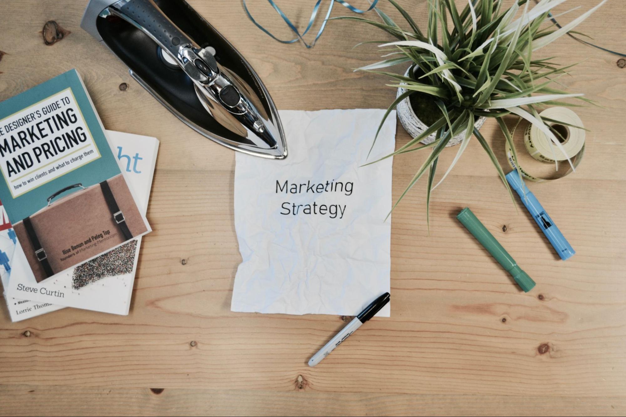 A wrinkled paper labled Marketing Strategy lays on a table next to an iron, representing Darren and Mike’s marketing advice