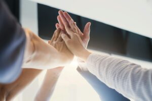 A group of hands joining in a high-five, symbolizing teamwork and collaboration in building a successful Enagic MLM business through shared support and community efforts.