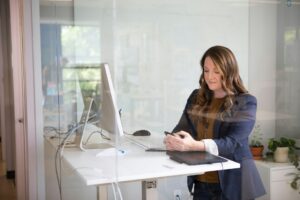 Professional woman in a modern office using her smartphone and working on a computer, symbolizing productivity and digital tools for building a successful online business.