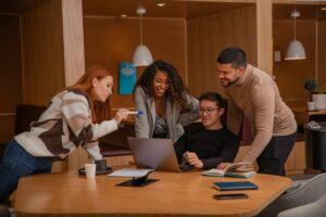 A diverse team of aspiring entrepreneurs collaborating on a business strategy around a laptop, embodying the principles of trust, communication, and shared vision emphasized by the Darren and Mike Dream Team.