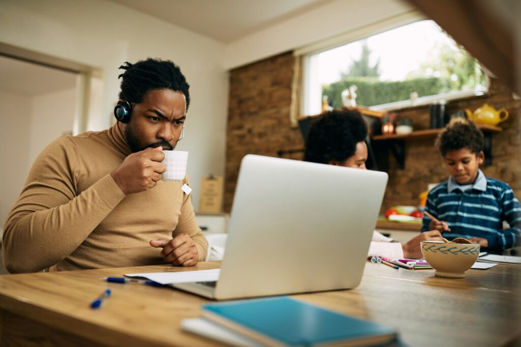 Focused entrepreneur working on a laptop while sipping tea at a home workspace, showcasing the balance of innovation, productivity, and family life. The Darren and Mike Way emphasizes empowering entrepreneurs to take control of their futures and create meaningful success.