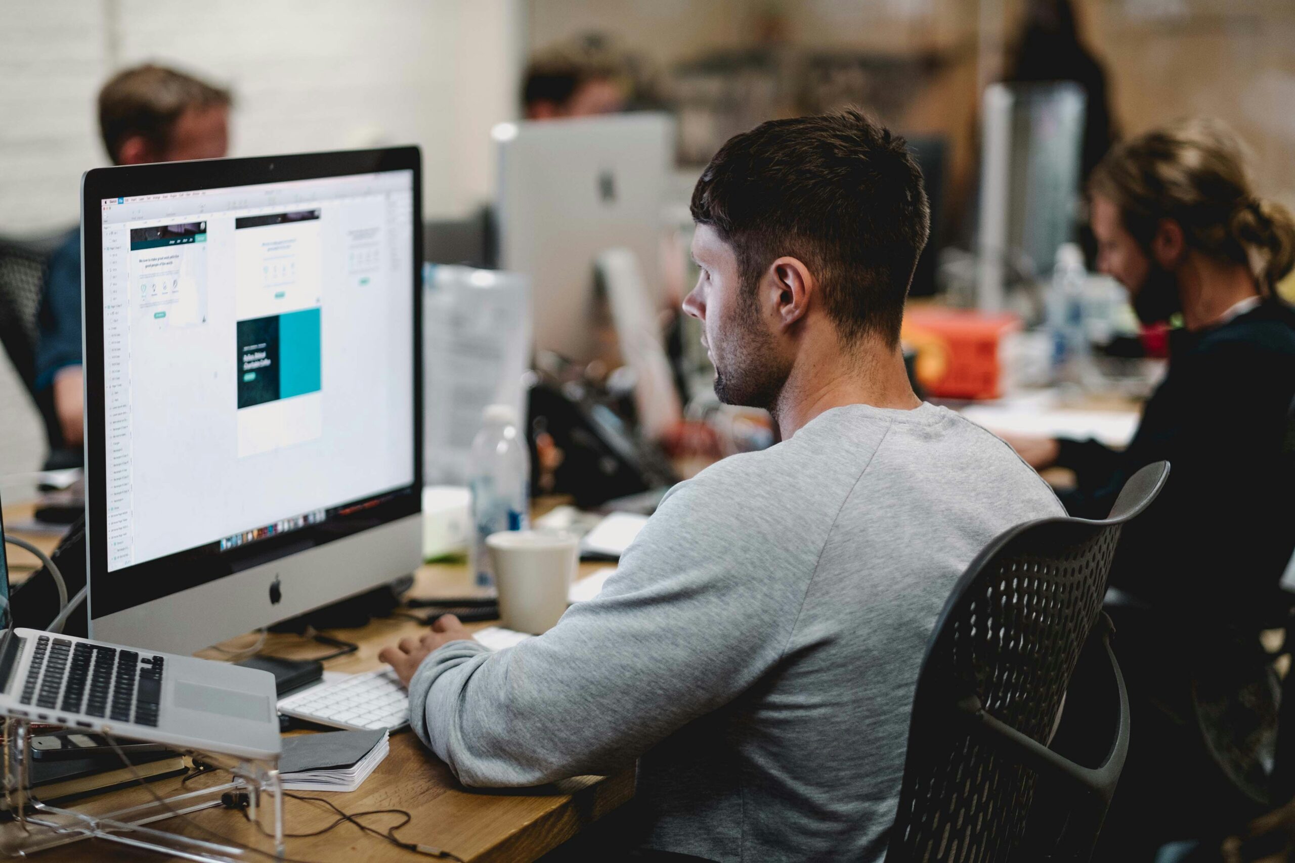 A person focused on their work on an iMac in a collaborative office space. This represents the dedication and innovation of the Darren and Mike Dream Team.