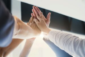 Close-up of diverse hands joining in a high five—symbolizing unity, mentorship, and the supportive community behind Darren and Mike’s Dream Team empowering underdogs to become digital leaders.