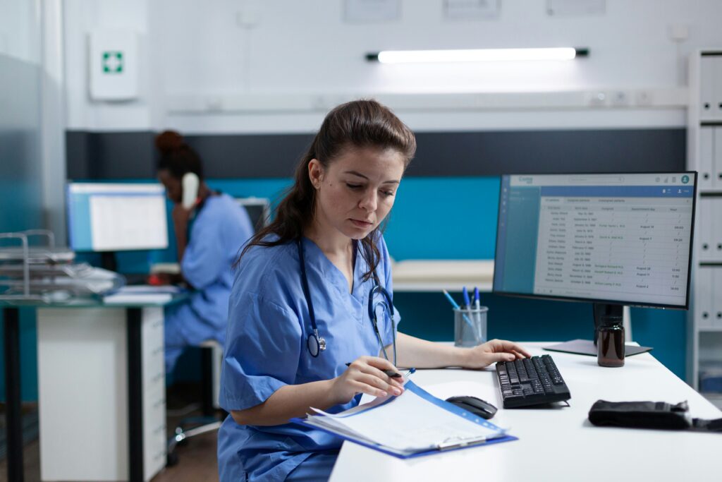 Nurse in blue scrubs with a stethoscope working at a hospital desk, exploring side hustles for nurses to build extra income