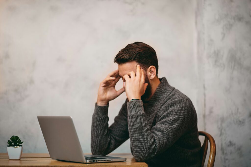 Frustrated entrepreneur with head in hands at a laptop, struggling to gain momentum in his online business