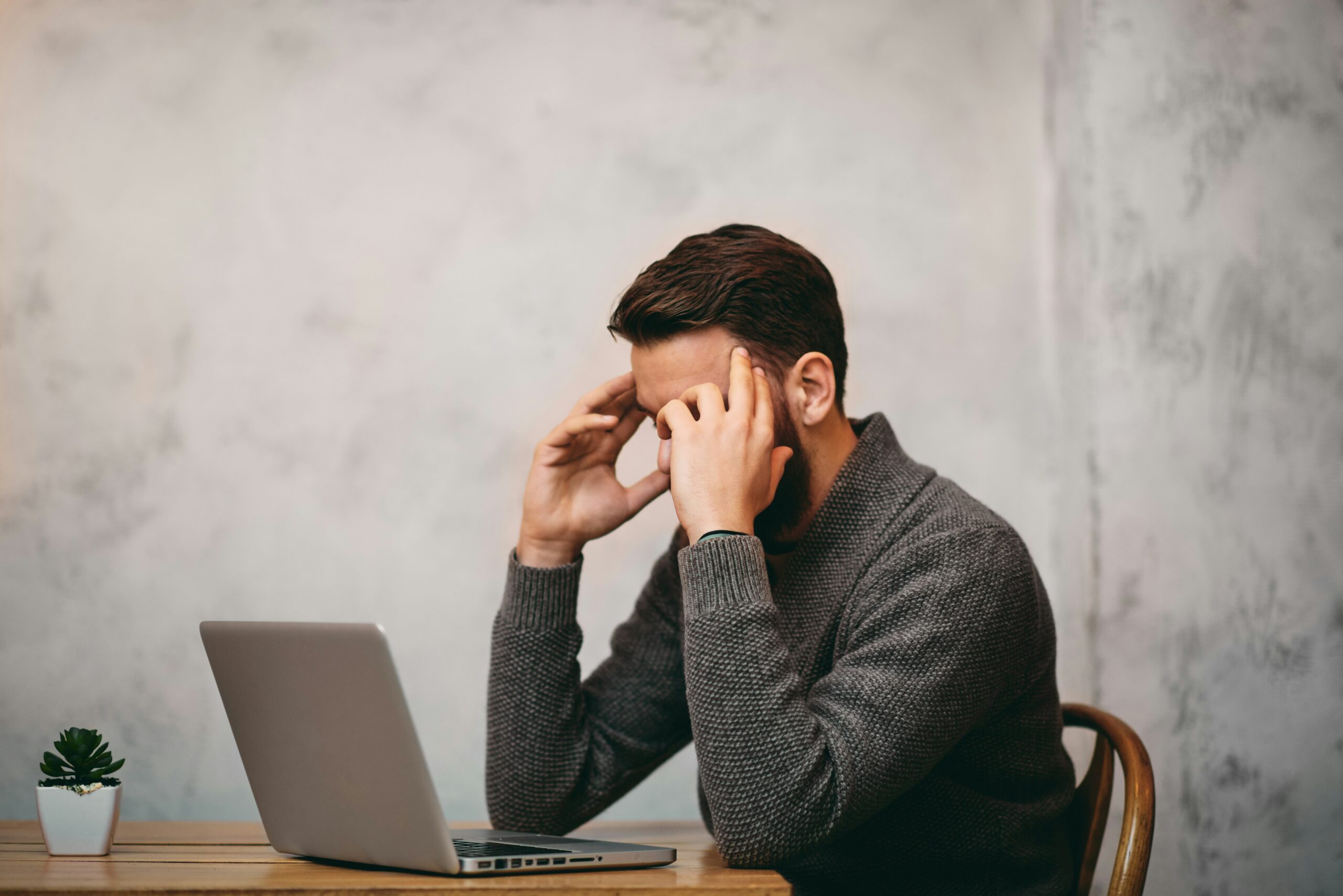 Frustrated entrepreneur with head in hands at a laptop, struggling to gain momentum in his online business
