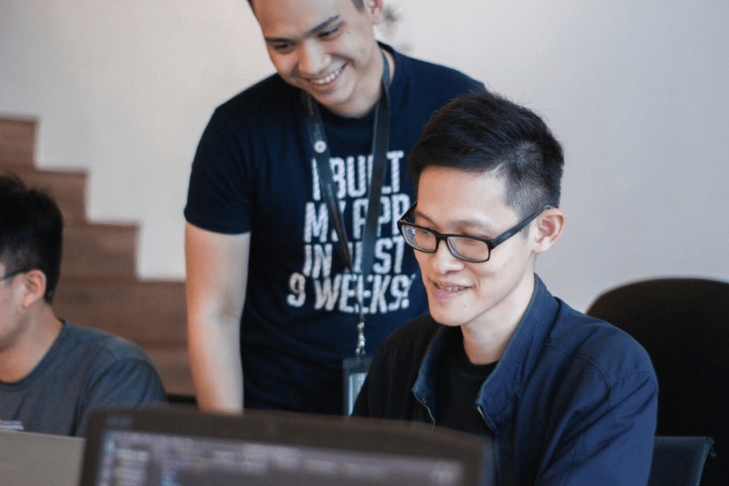 Smiling mentor guiding a team member at a computer, representing the role of a business coach for online business success and growth.