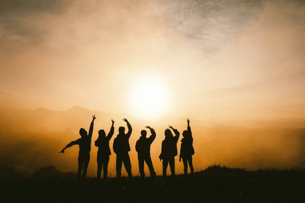 Silhouettes of people raising hands at sunrise, symbolizing unity and support among members building digital businesses.