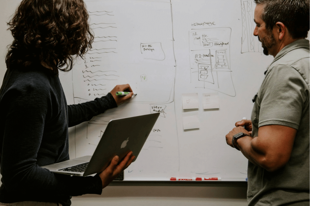 Two people collaborating on effective communication strategies, using a whiteboard to develop business communication skills for success.