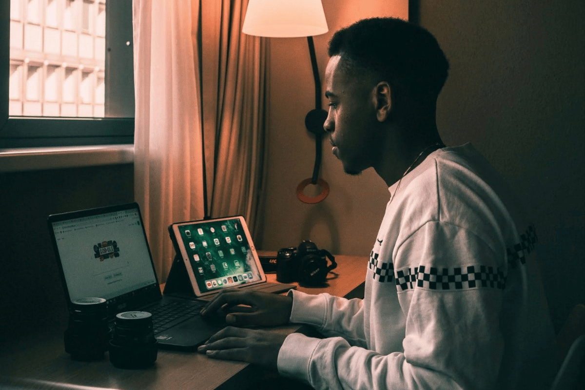 Young man working on digital side hustle from home using laptop and tablet in a remote workspace