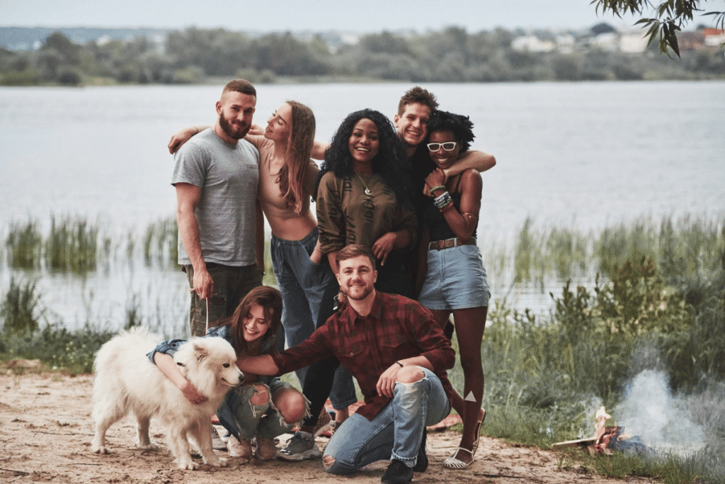  Diverse group of friends smiling by a lake, symbolizing the supportive and empowering spirit of the community of underdogs in digital entrepreneurship.
